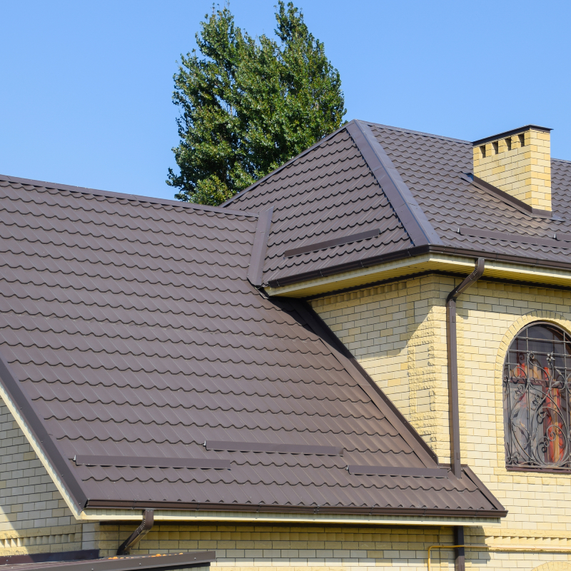House of yellow brick and brown corrugated roof made of metal. Lattices on the windows