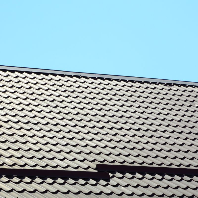 A fragment of a roof from a metal tile of dark red color. Quality Roofing .
